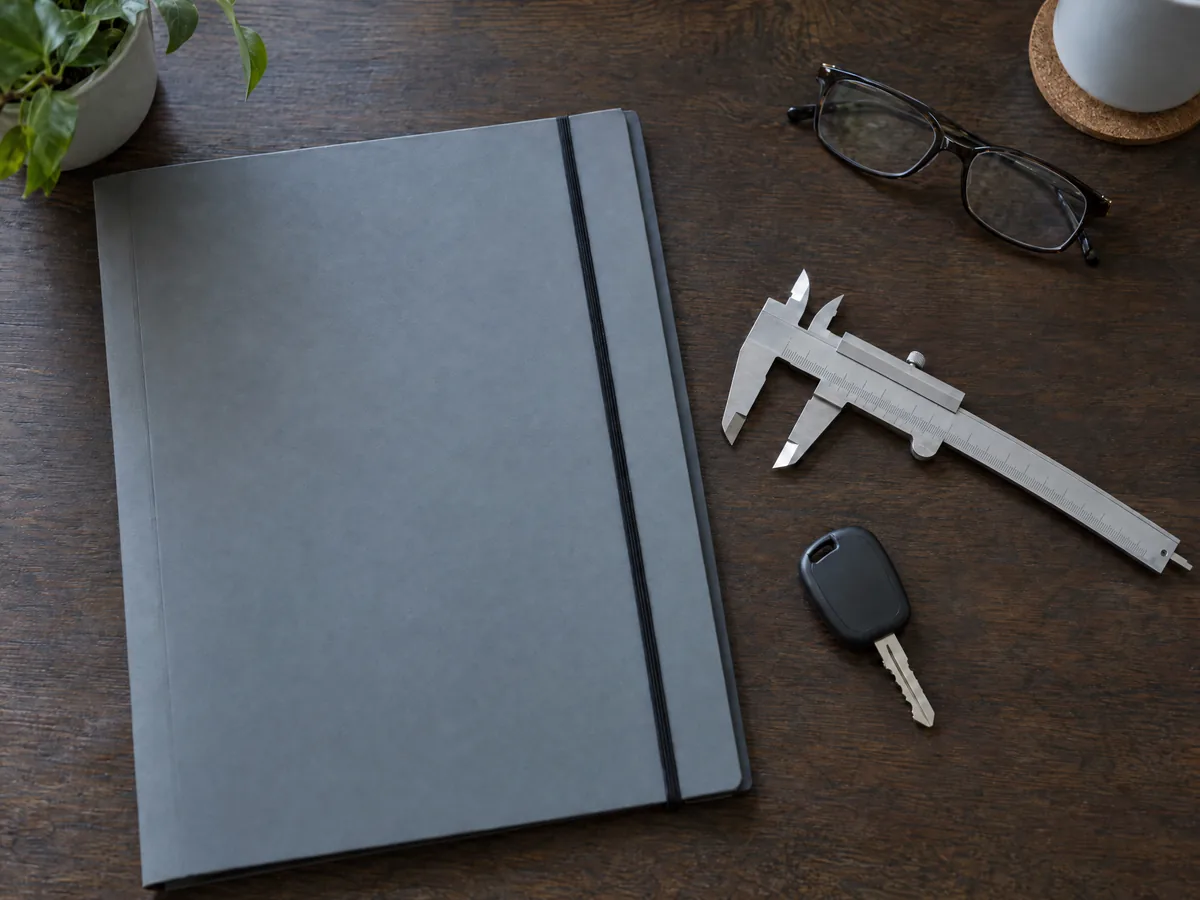 Gutachtenmappe mit Messschieber, Fahrzeugschlüssel und Brille auf einem Schreibtisch
